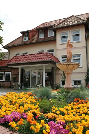 Un edificio con techo de tejas rojas, una estatua en el jardín y una variedad de flores.