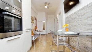 Una cocina moderna con horno empotrado, comedor con sillas traslúcidas y salpicadero de azulejos blancos.