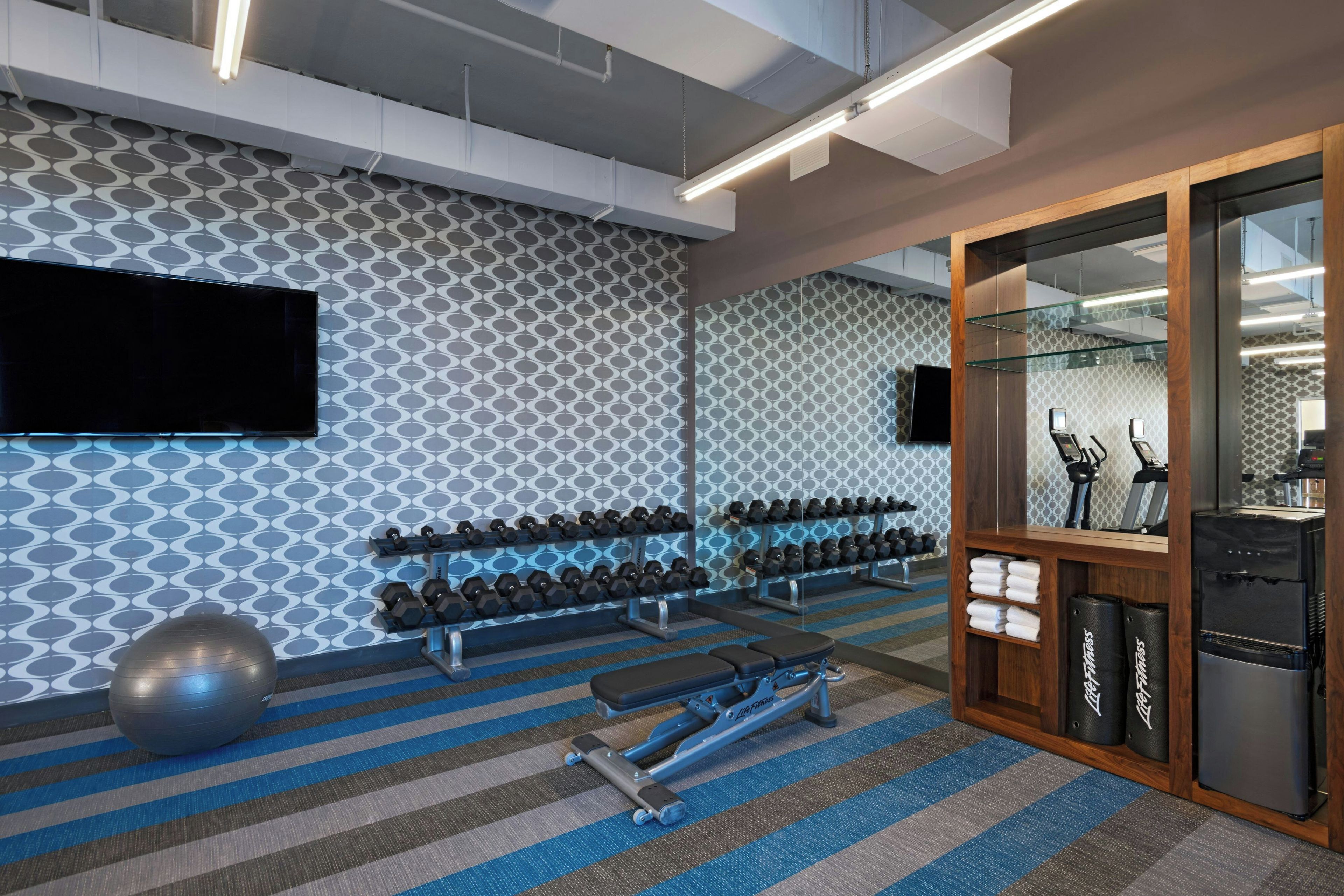 Un gimnasio con equipo de ejercicio, un televisor y un espejo grande.