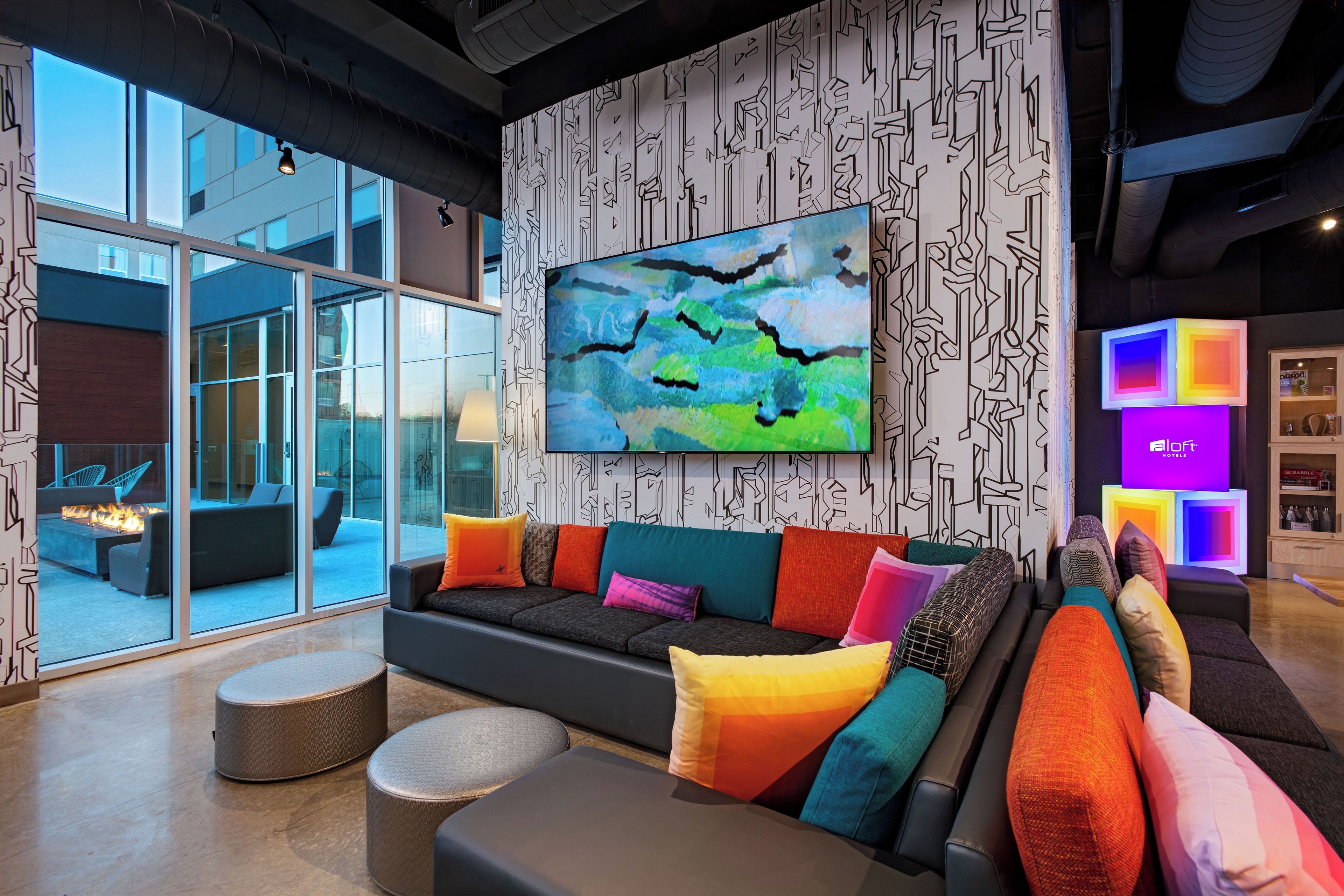 A modern hotel lobby with a large window, a sectional sofa with colorful cushions, and a large abstract painting on the wall.