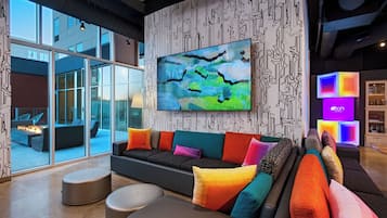 Un moderno vestíbulo de hotel con un ventanal grande, un sofá modular con cojines de colores y un cuadro abstracto de gran tamaño en la pared.