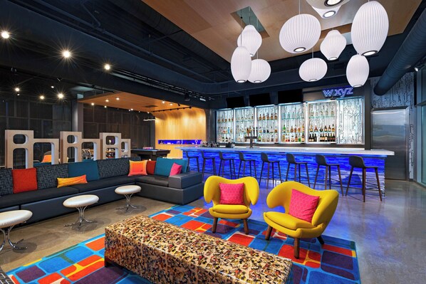 A modern lounge area with a bar, seating, and a colorful rug. - Aloft by Marriott Waco Downtown (Waco)