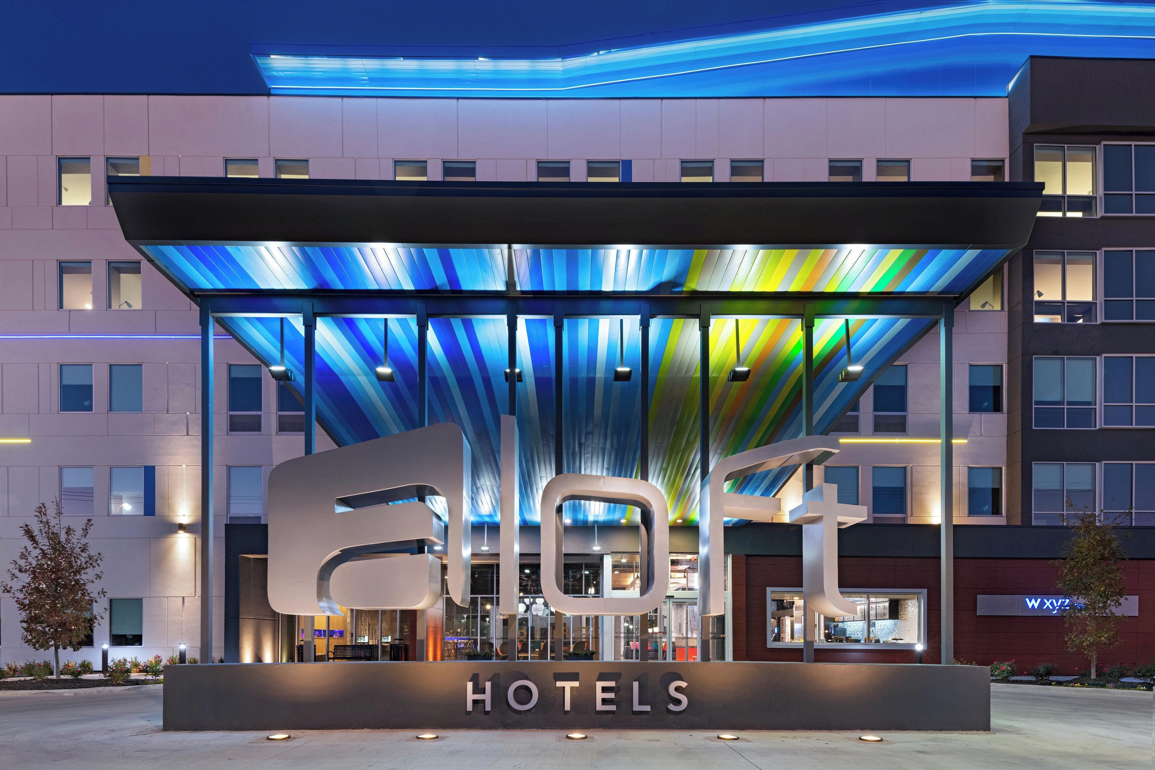 Een hotelentree met een modern ontwerp, met een grote verlichte luifel en een opvallend 'HOTELS' bord.