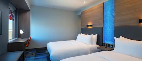 A hotel room with two beds, a desk, a chair, and a large window.