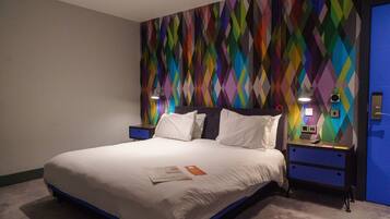 Una habitación de hotel con una cama grande, una mesita de noche, una lámpara de pared y una puerta con un panel azul.