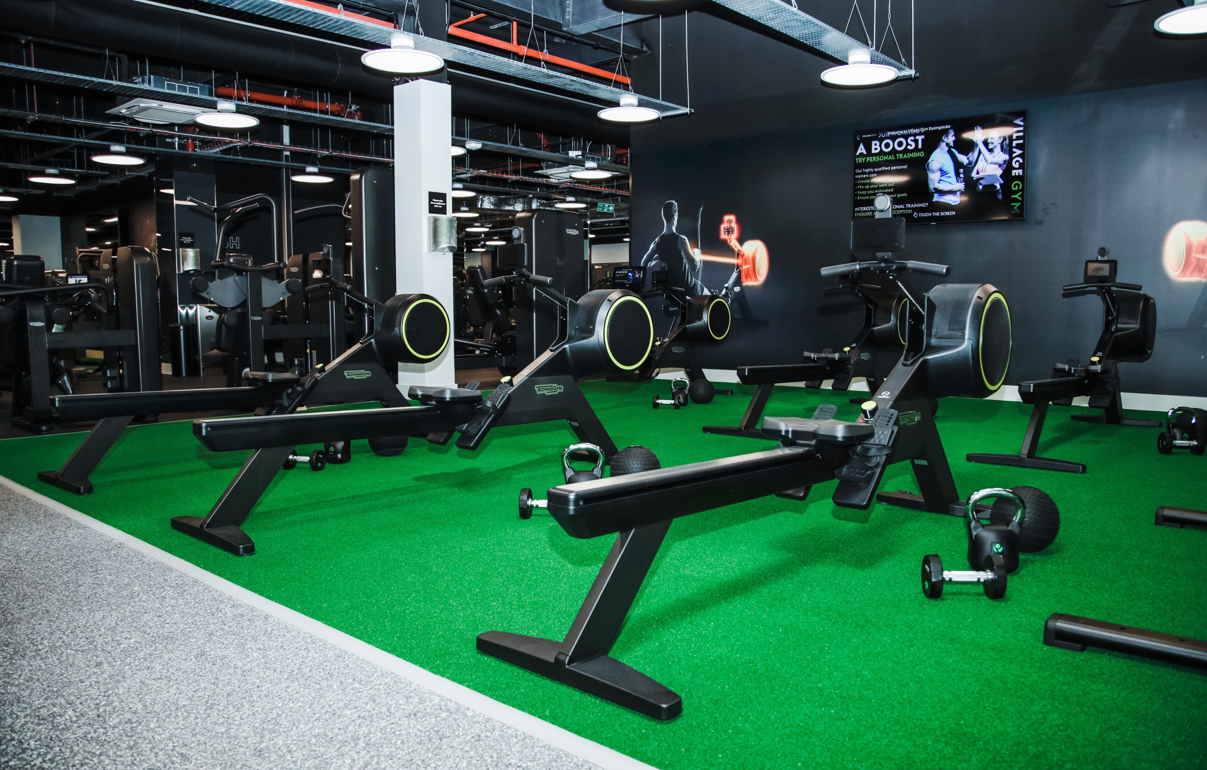 A gym with various exercise equipment, a green floor, and a TV screen displaying a workout video.