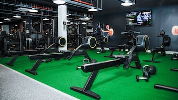 A gym with various exercise equipment, a green floor, and a TV screen displaying a workout video.