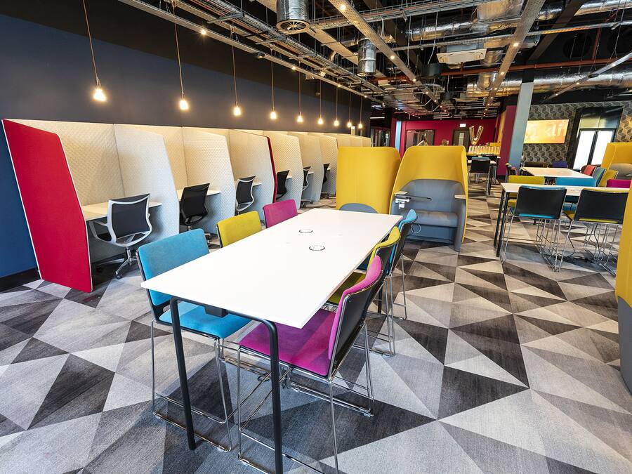 Une salle de conférence moderne, dotée d’une table blanche, de chaises colorées et d’un sol orné de motifs géométriques.
