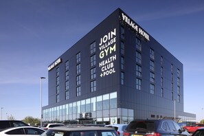 A modern building with a sign advertising a gym, health club, and pool. - Village Hotel Basingstoke (Basingstoke)