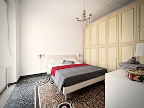 A bedroom with a bed, a wardrobe, a chandelier, and a patterned rug. - Panoramica Centrale Casa Rivoli (Genoa)