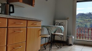 Una cocina con armarios de madera, una mesa con una silla, un radiador y vistas a un bosque por la ventana.