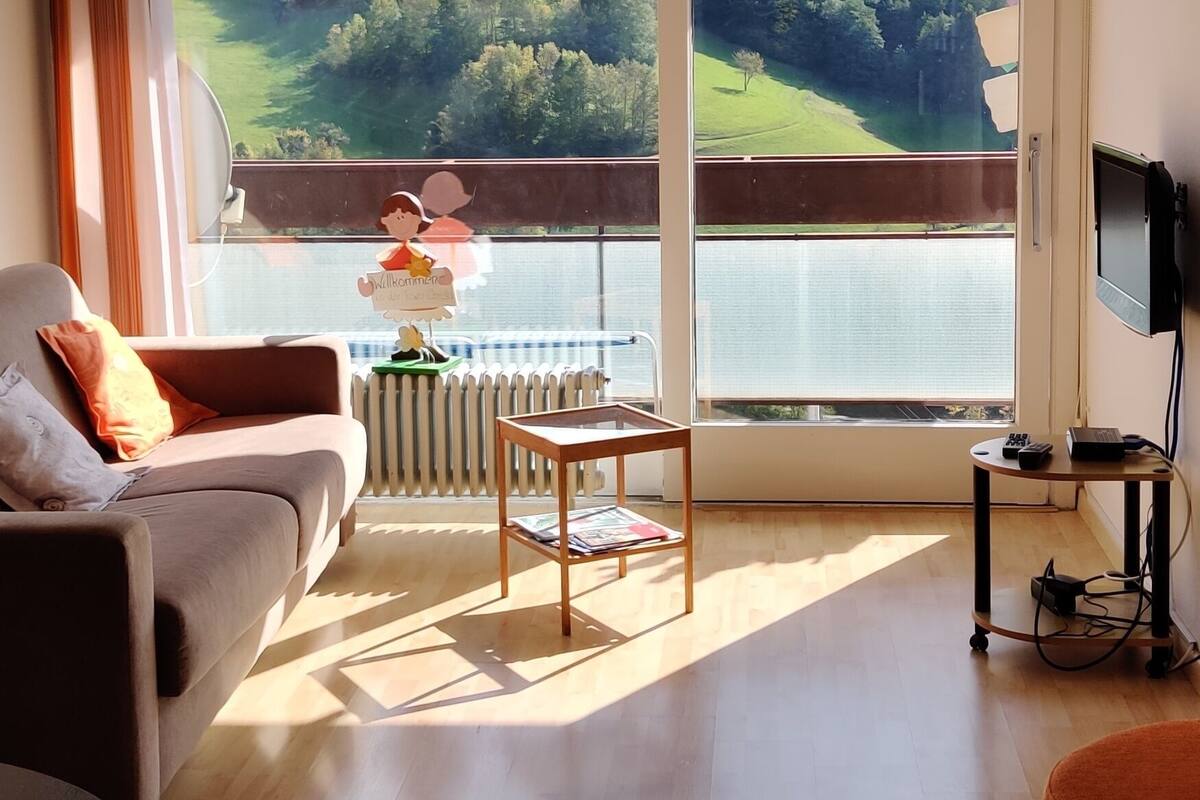A living room with a large window, a sofa, a coffee table, and a TV stand.