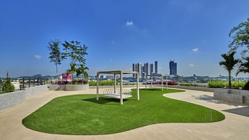 A rooftop garden with a swing set, a view of the city skyline, and a paved walkway.