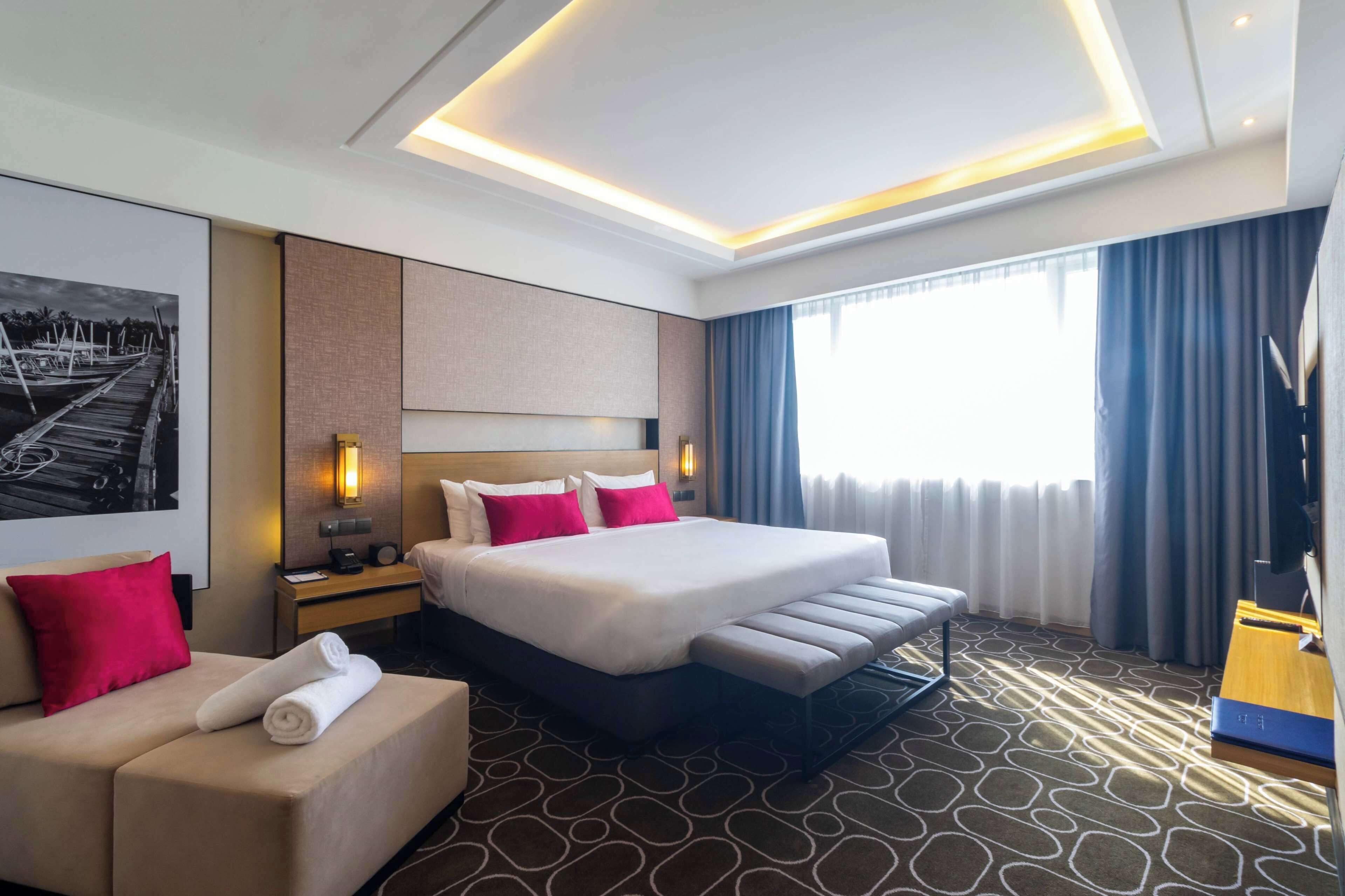 Een hotelkamer met een groot bed, een bank, een bureau en een groot raam met gordijnen.