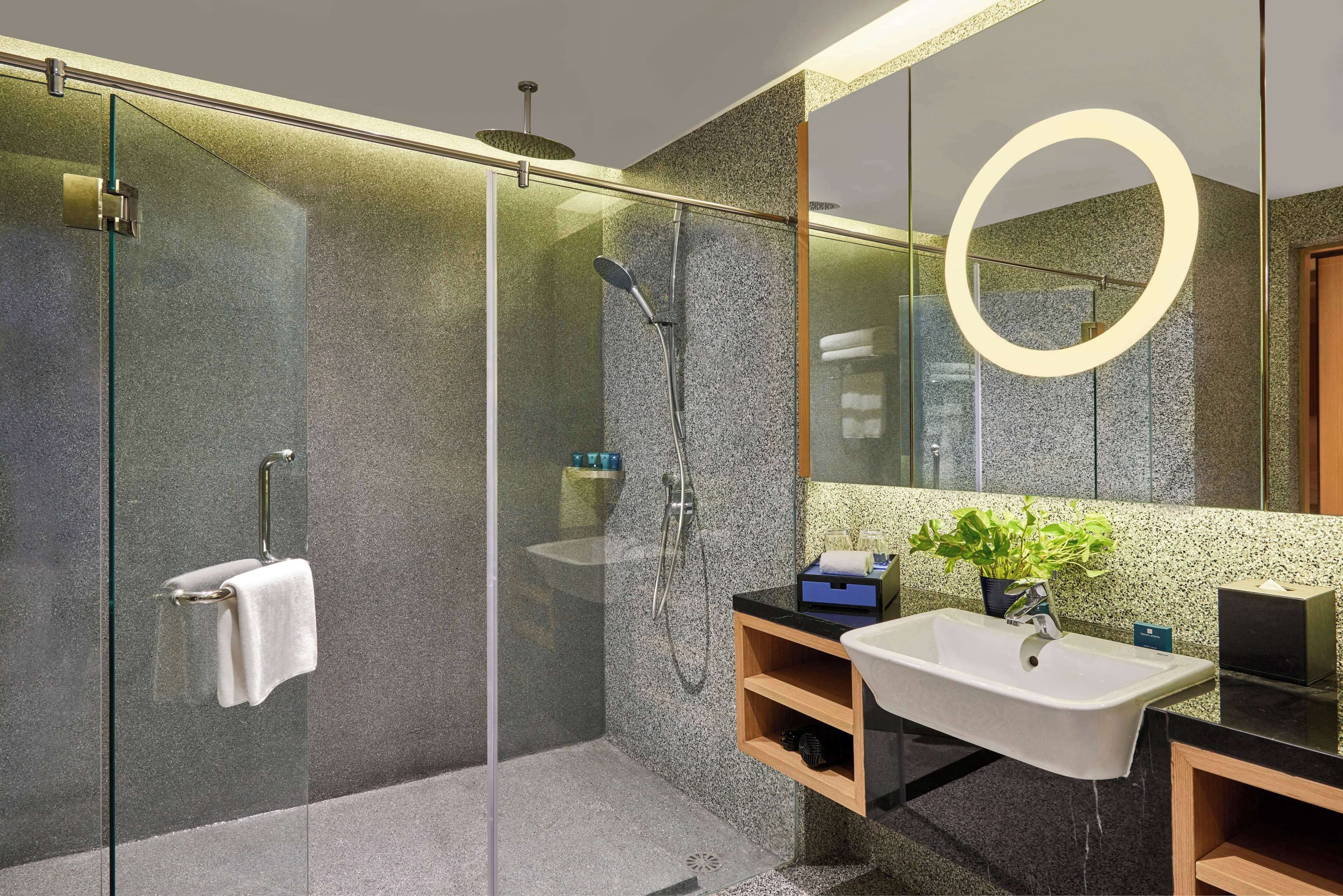 Un baño moderno con ducha de vidrio, un lavamanos con espejo y una planta en maceta.
