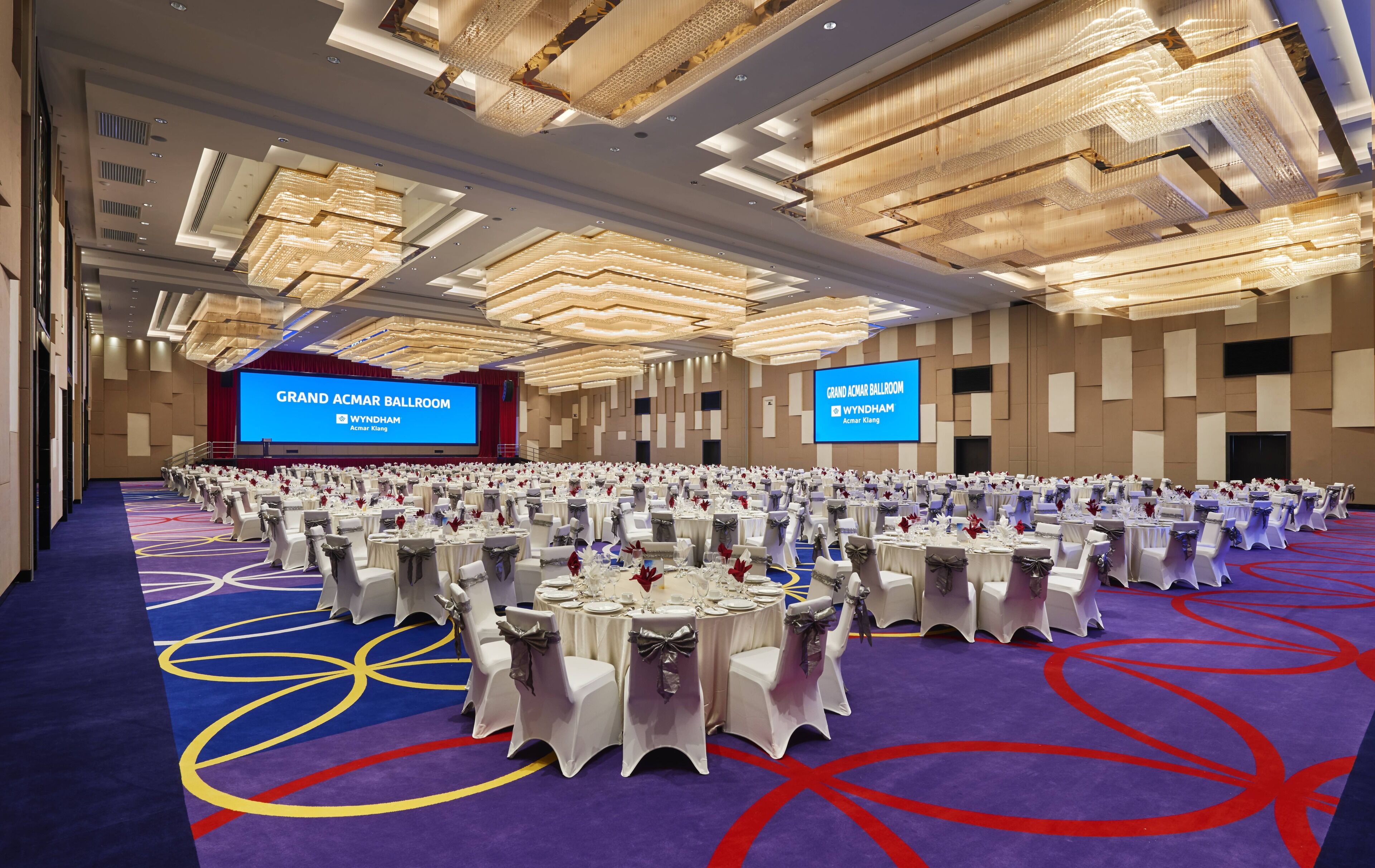 A large ballroom with round tables and chairs, a stage, and a large screen displaying the name 'Grand Acamar Ballroom'.