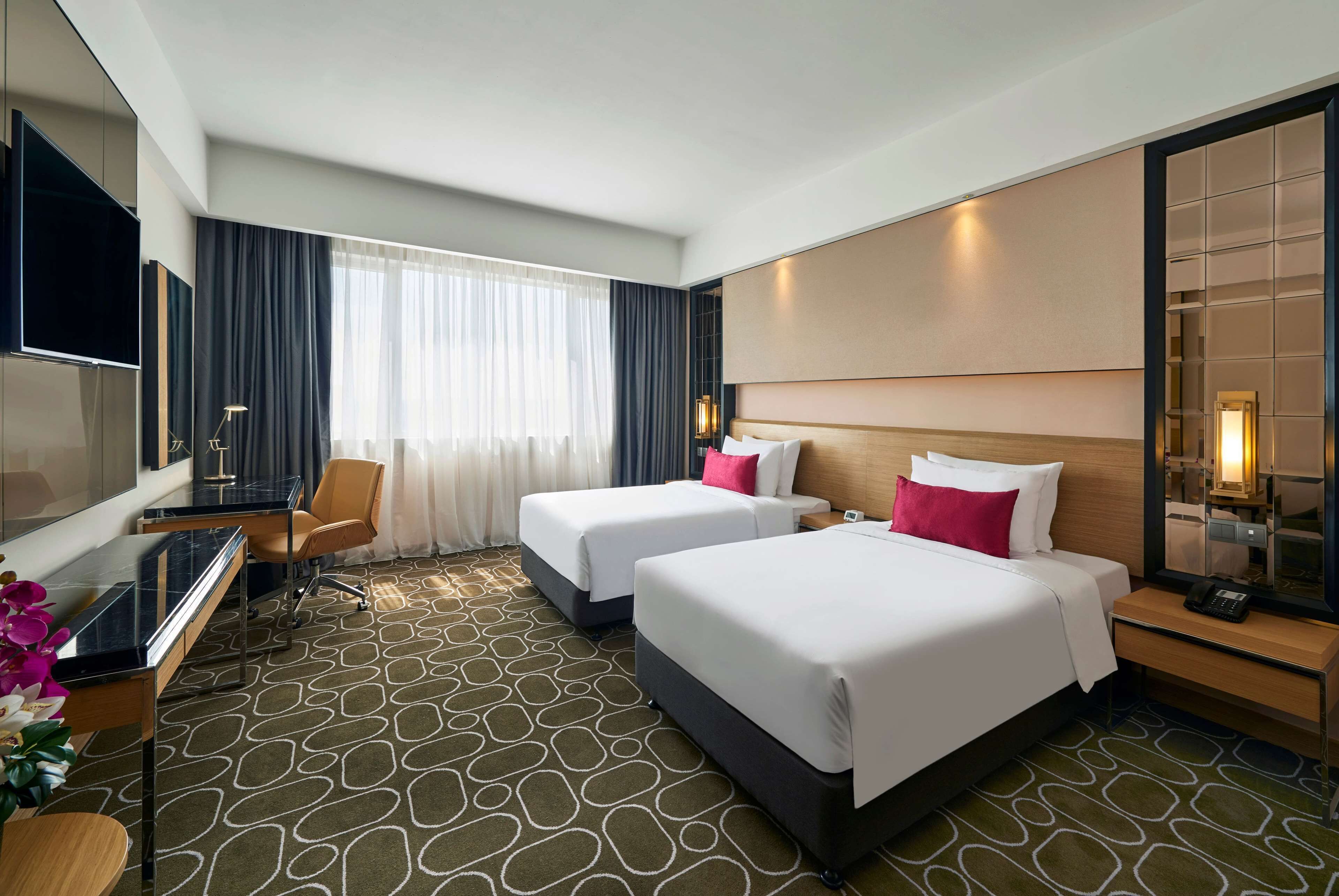A hotel room with two beds, a desk with a computer, a TV, and a large mirror.