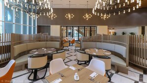 Un comedor moderno con mesas redondas y asientos acolchados, con luminarias contemporáneas y vistas a través de grandes ventanales.
