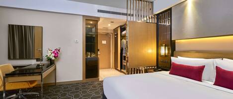 A hotel room with a bed, desk, chair, and a small table with a vase of flowers.