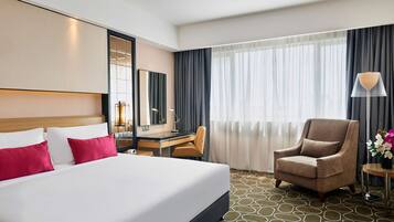 A hotel room with a large bed, a desk, a chair, and a window with curtains.