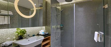 A modern bathroom with a glass-enclosed shower, a freestanding sink, and a large mirror with a circular frame.