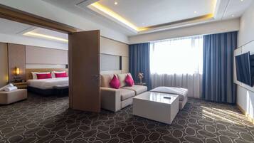 A modern hotel room with a bed, sofa, and coffee table, a TV, and a large window with curtains.