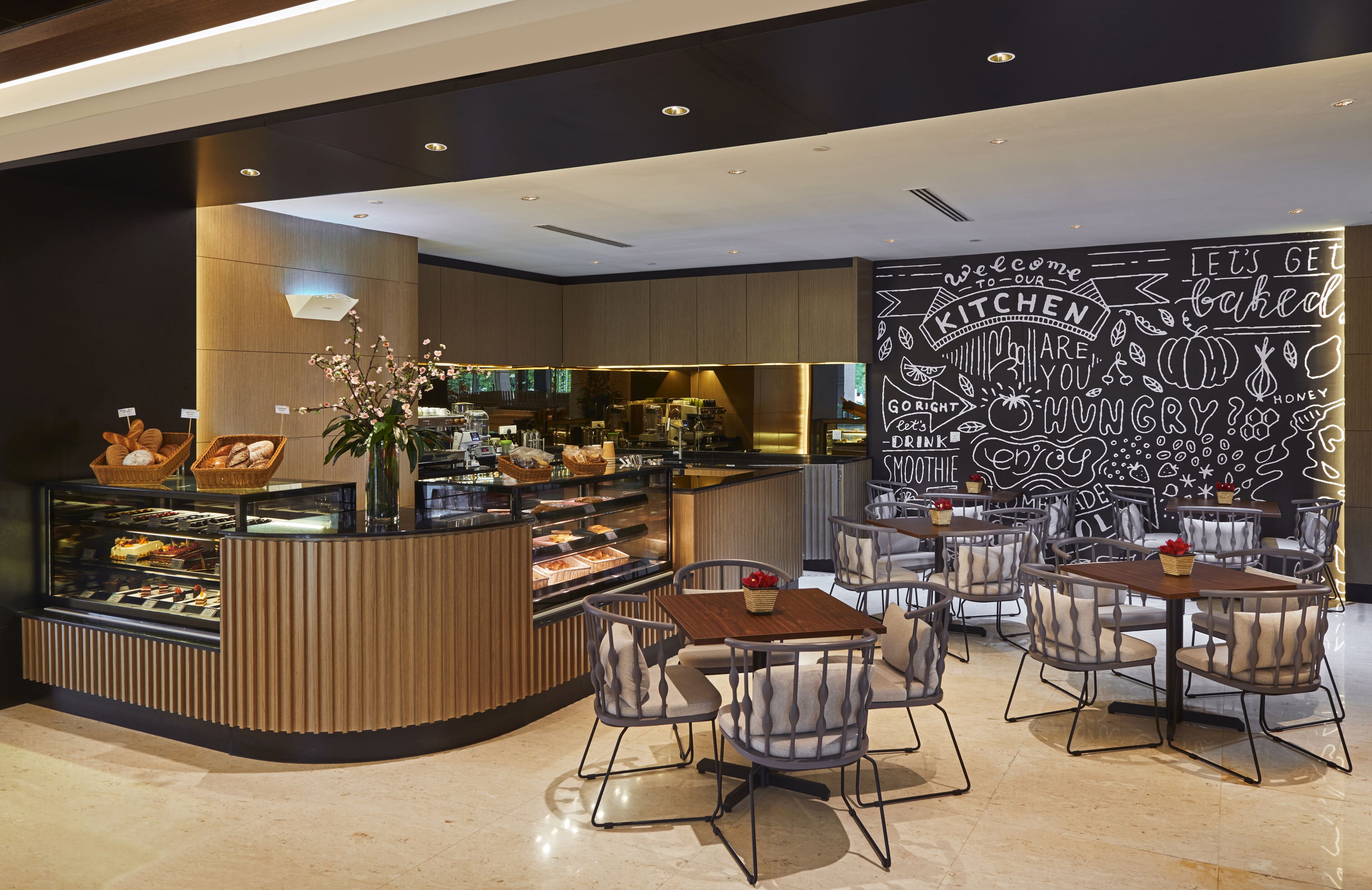 A modern cafe with a central counter displaying pastries and a seating area with tables and chairs.