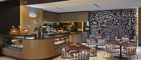 A modern cafe with a central counter displaying pastries and a seating area with tables and chairs.