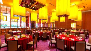 Een feestzaal met ronde tafels gedekt voor een diner, met rode tafelkleden en witte servetten.