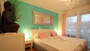 Quarto com cama, mesa de cabeceira, estátua de Buda, espelho e janela com cortinas.