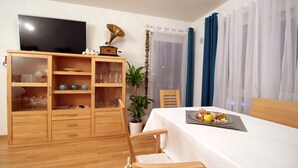 Quarto com cama, armário de madeira com portas de vidro, televisão, planta e mesa com um prato de comida.