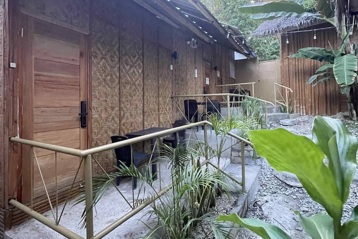 A wooden building with a thatched roof, surrounded by tropical plants and a gravel pathway.