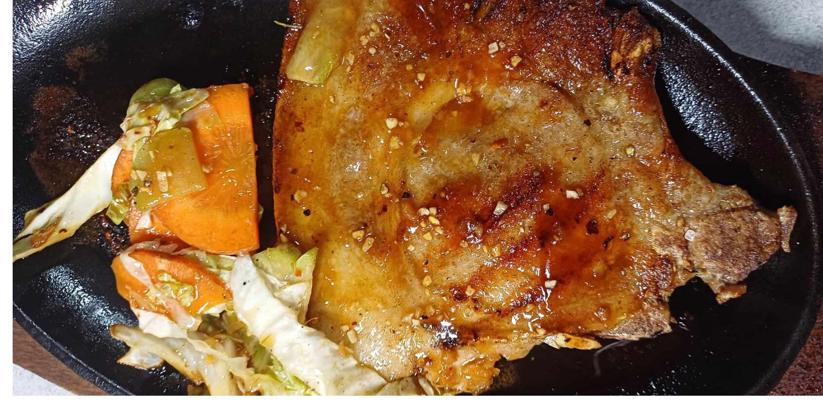 Une côte de porc grillée, accompagnée de légumes, servie dans une poêle noire.