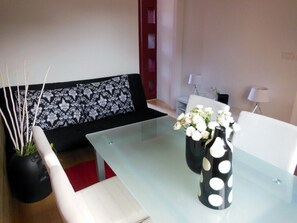 A modern living room with a glass coffee table, a black and white patterned sofa, and a vase with white flowers.