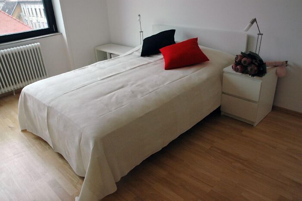 Une chambre à coucher avec un lit, une table de chevet, une lampe et une fenêtre.