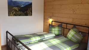 A bedroom with a wooden headboard, a bed with green and gray checkered bedding, and a mountain landscape painting on the wall. - Arrive and feel good in the exclusive and modern Chalet Weitsee (Reit im Winkl)