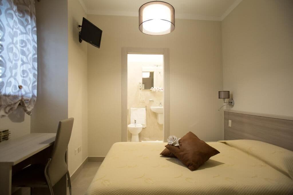 Ein Hotelzimmer mit Bett, Schreibtisch, Stuhl, an der Wand montiertem Fernseher und angrenzendem Badezimmer.