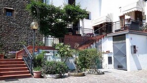 Un patio con escalones de piedra, plantas en macetas y un edificio con fachada blanca y un balcón.