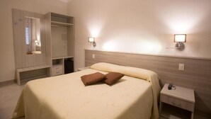 Habitación de hotel con cama, mesitas de noche, armario y luces fijadas a la pared.