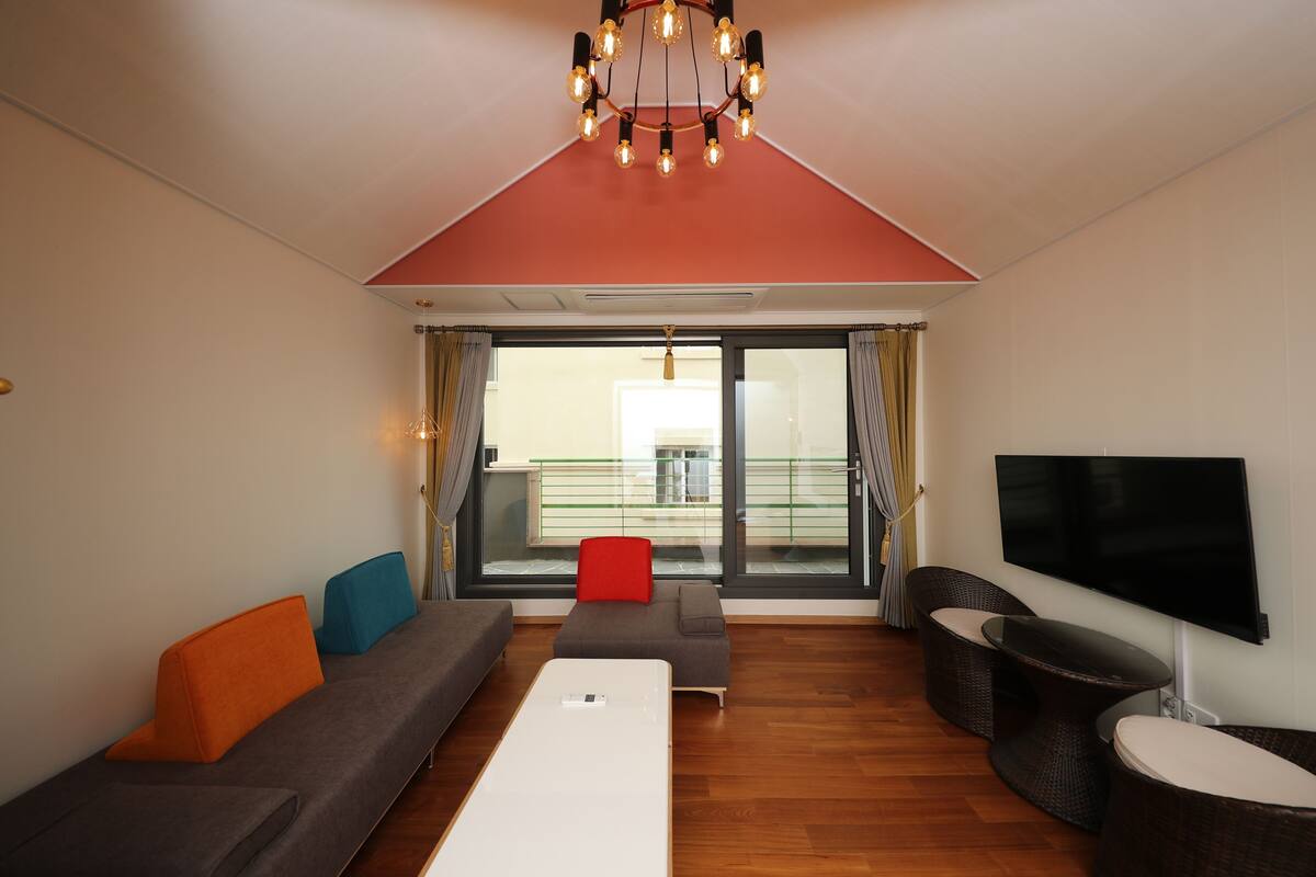 A modern living room with a sofa, ottoman, and a flat-screen TV.