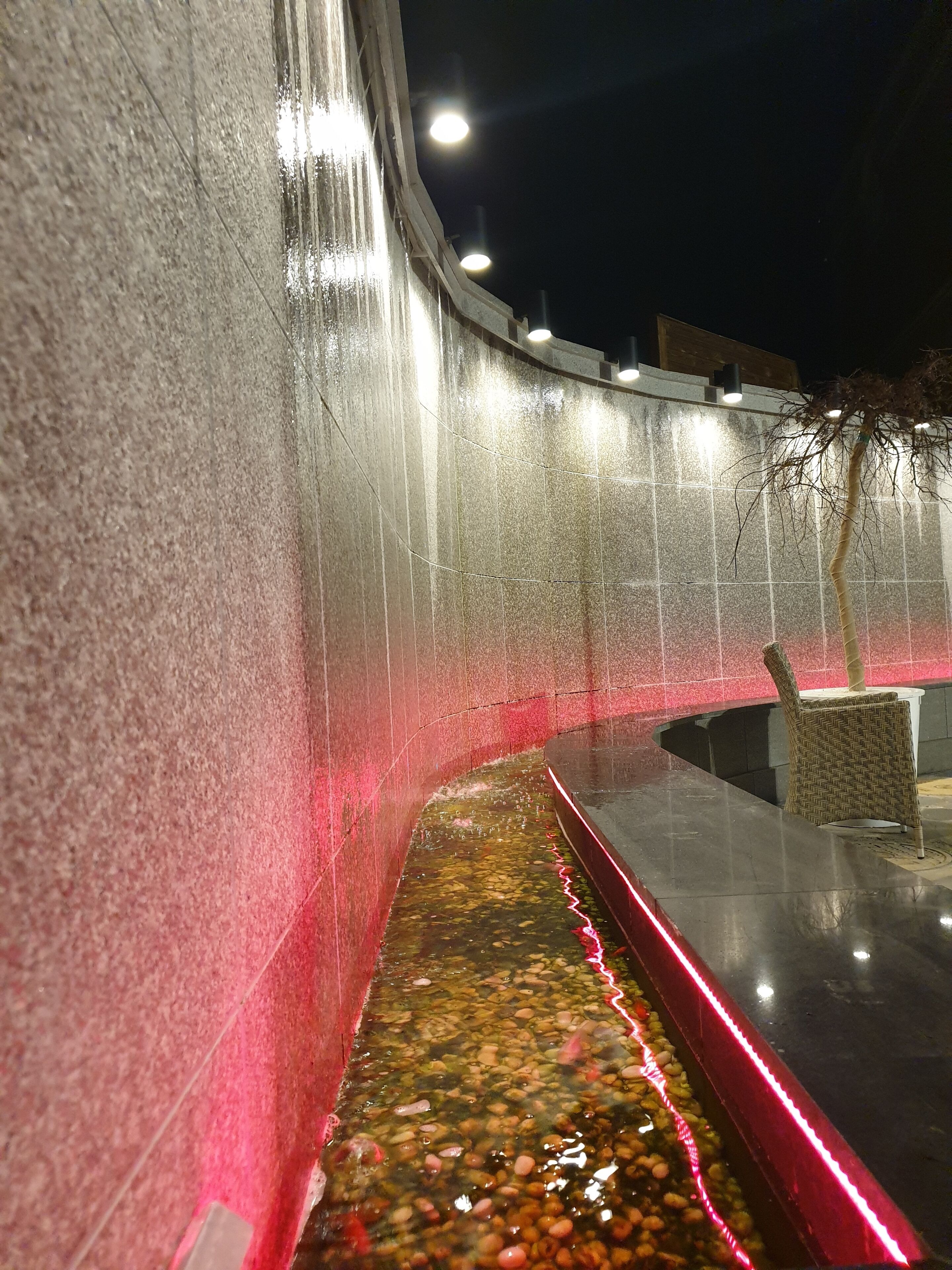 Ein abendliches Wasserspiel mit einer gewölbten Wand und einem schmalen Wasserstrahl.