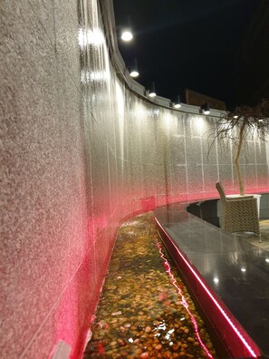 Una fuente nocturna con un muro curvo y un estrecho hilo de agua.