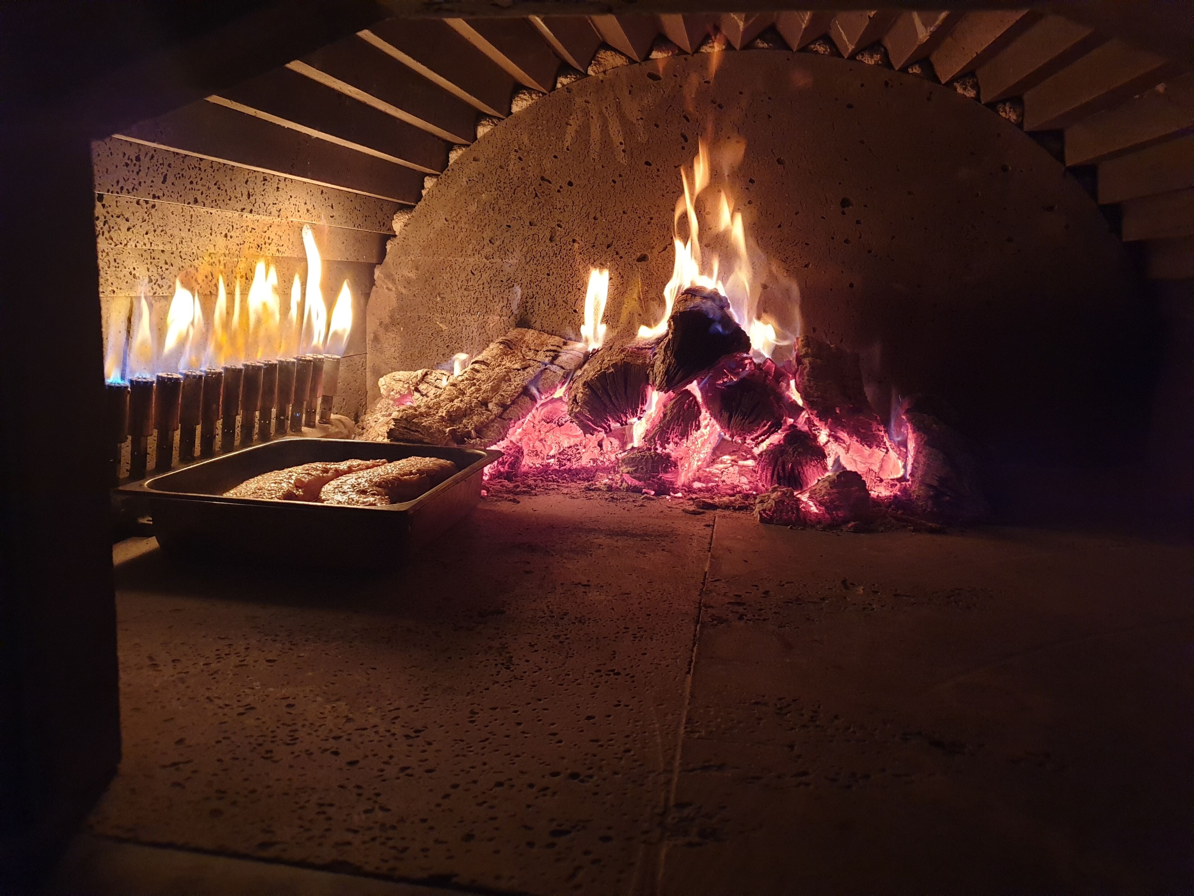 A pizza oven with flames and wood logs inside.