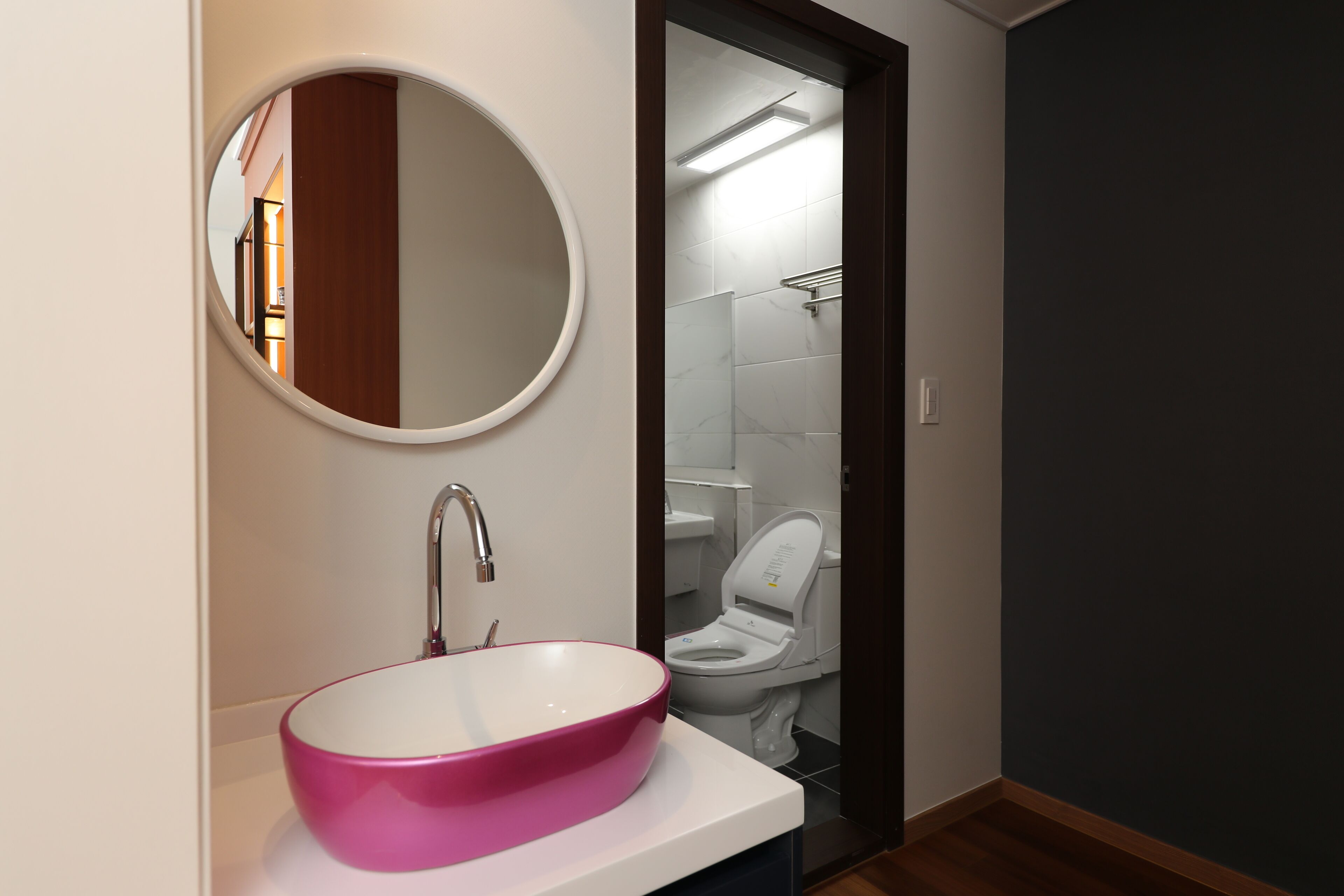 Un baño con un espejo redondo, un lavamanos rosa y un inodoro.