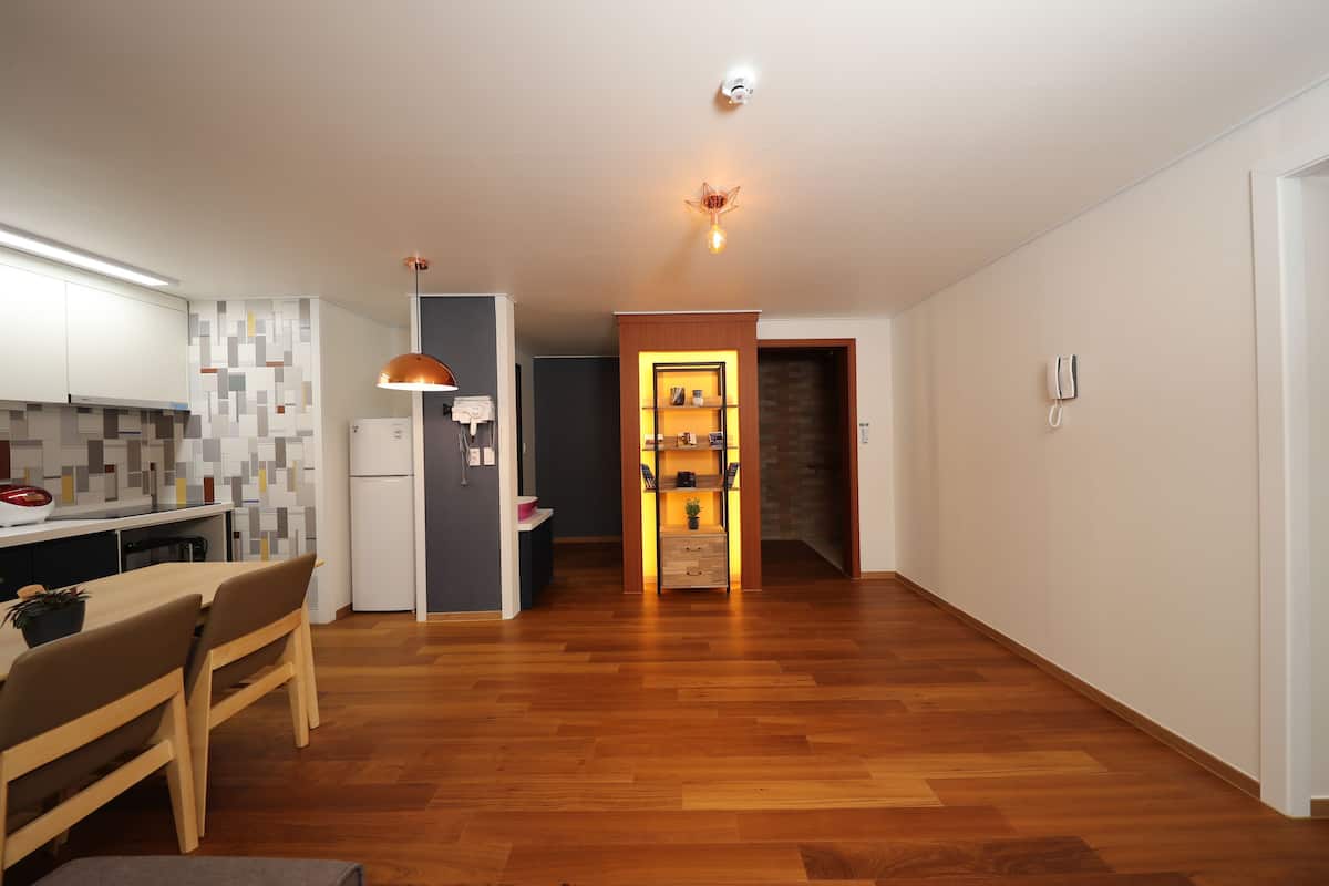 A modern kitchen with wooden flooring, a dining area with a table and chairs, and a hallway leading to a living space.