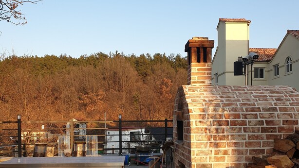 A stone patio with a brick oven and a metal table with cooking utensils. - Buyeo Park Art Villas (Buyeo)