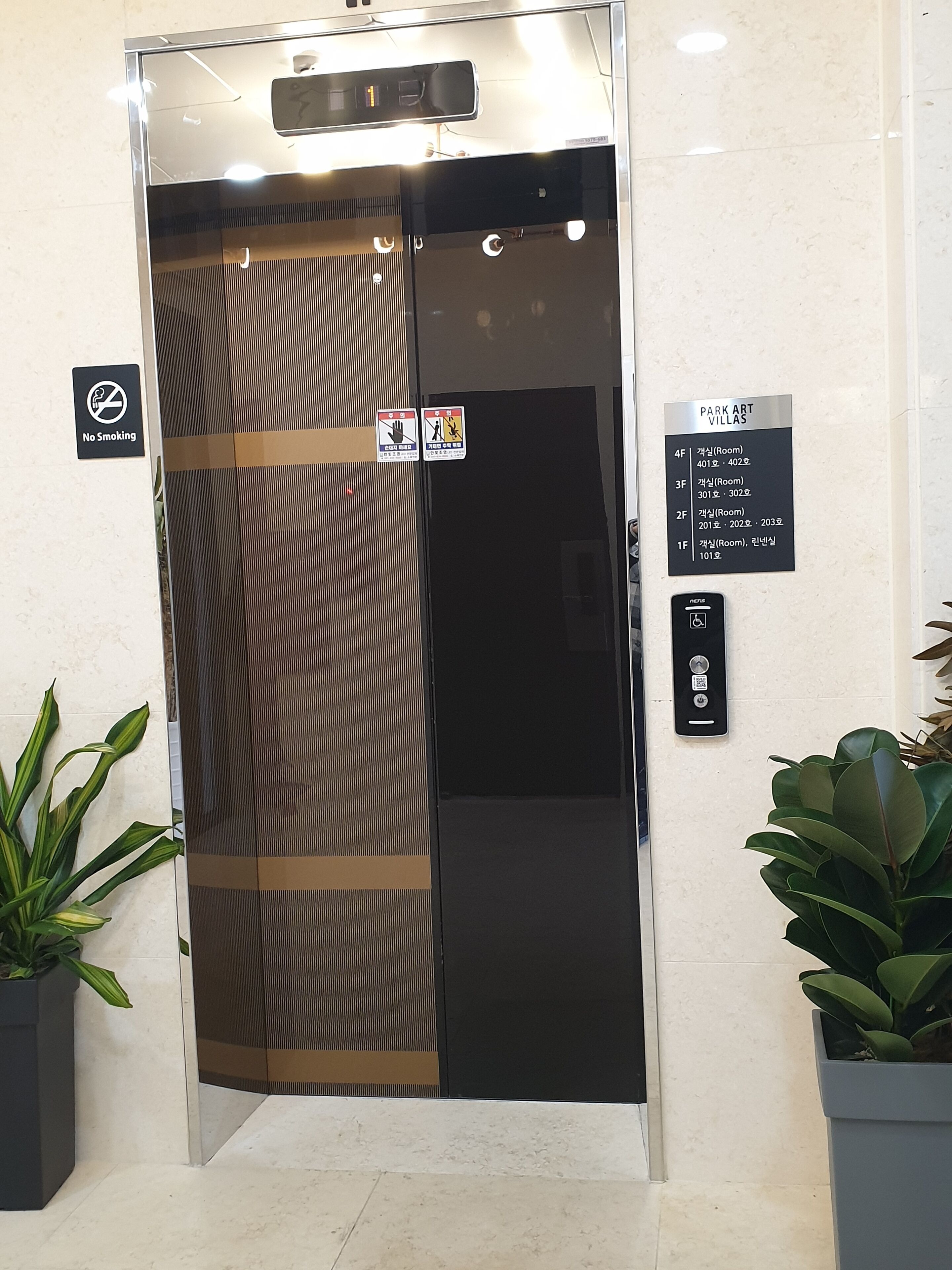 Een lift met een rookverbodsbord, een bord met 'Park Art Villas' en een paneel om de verdiepingen te selecteren.