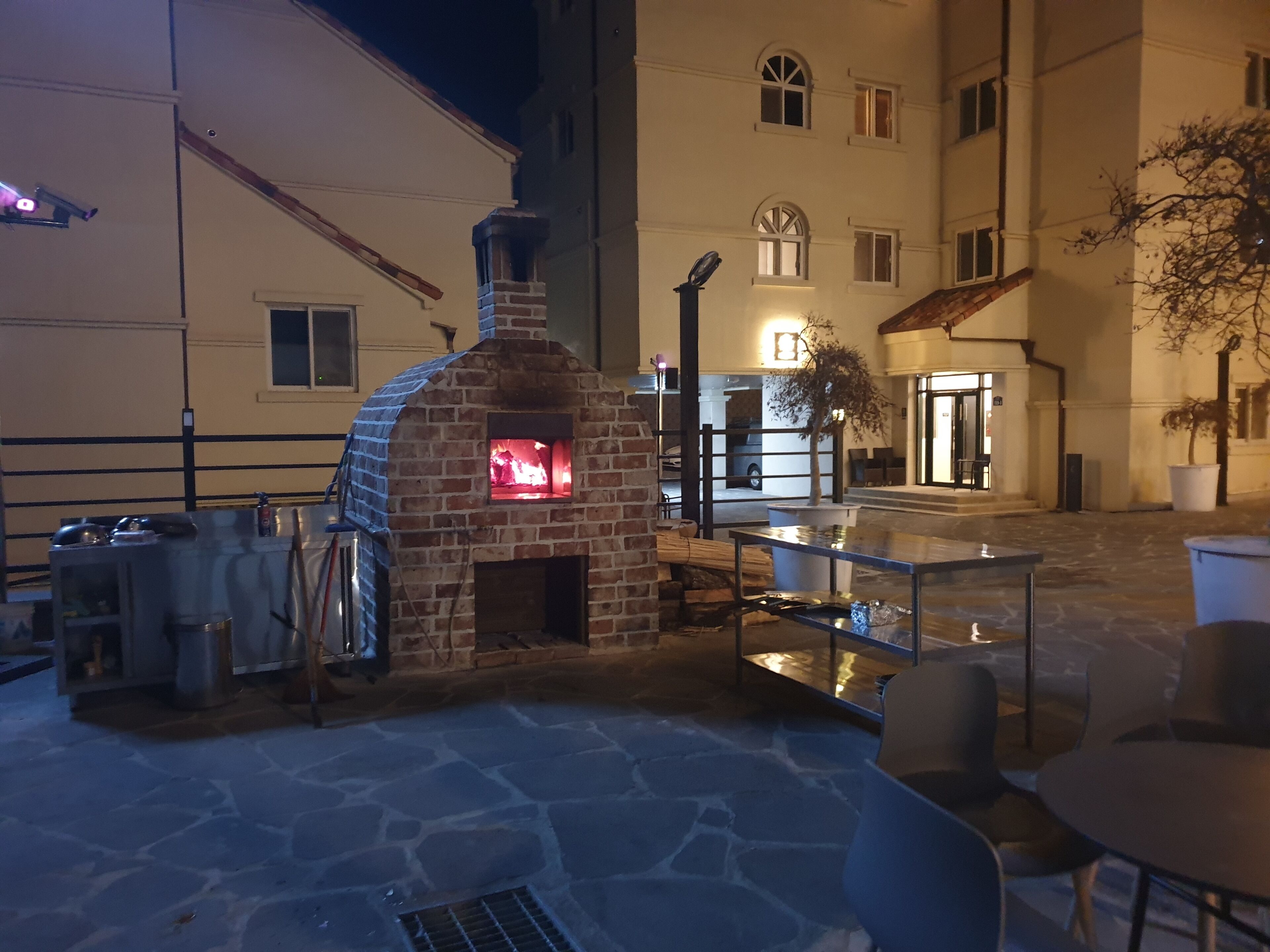 An outdoor patio area with a brick oven, stone flooring, and outdoor seating.