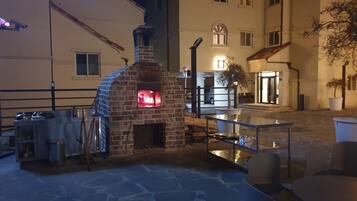 An outdoor patio area with a brick oven, stone flooring, and outdoor seating.