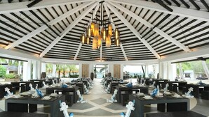 A spacious indoor area with high ceilings and a central chandelier, featuring multiple dining tables and chairs arranged in rows. - Aqua Fun Hotel (Mariveles)